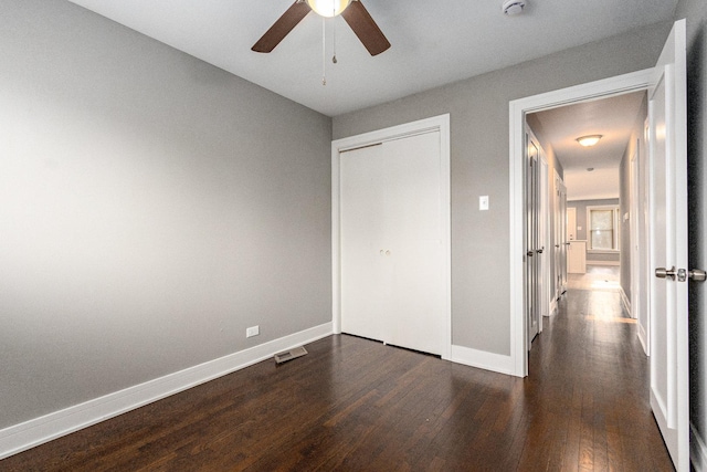 unfurnished bedroom with dark wood-type flooring, a closet, and ceiling fan