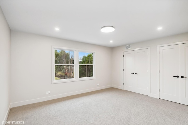 unfurnished bedroom featuring two closets and light colored carpet