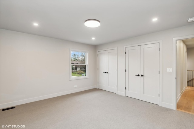 unfurnished bedroom featuring light carpet and two closets