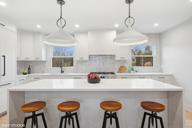 kitchen featuring pendant lighting, sink, premium range hood, stove, and a kitchen island