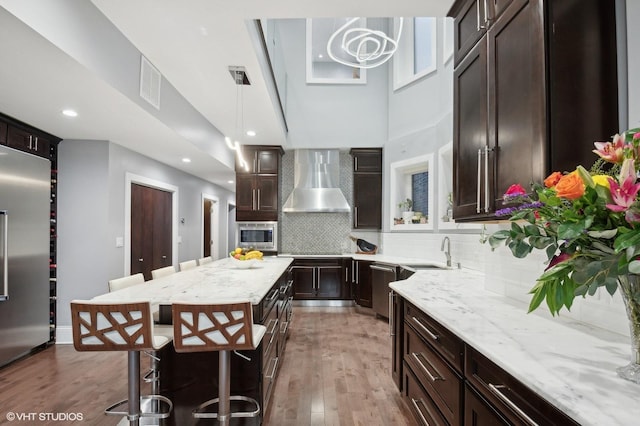 kitchen featuring wall chimney range hood, sink, a center island, built in appliances, and decorative light fixtures