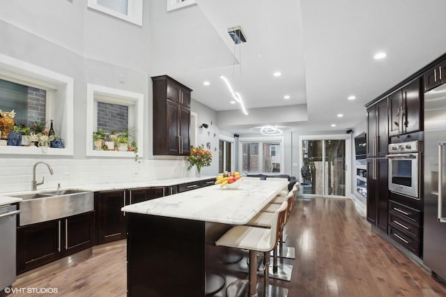 kitchen featuring dark wood-type flooring, a kitchen bar, a center island, hanging light fixtures, and stainless steel appliances