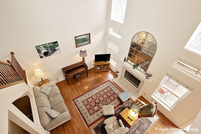 living room with a towering ceiling, plenty of natural light, a tile fireplace, and hardwood / wood-style flooring