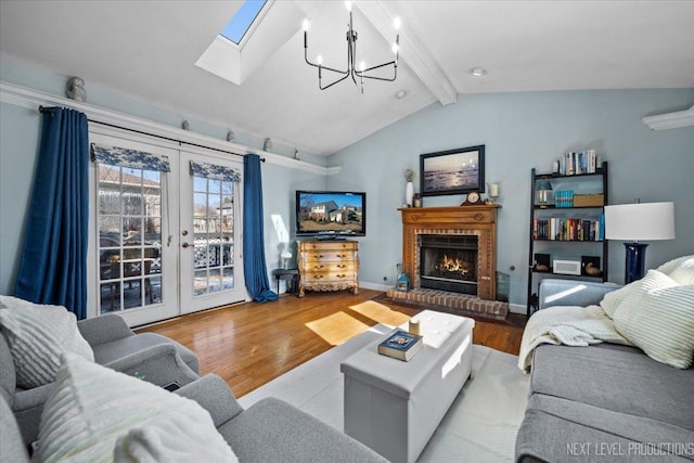 living room featuring french doors, vaulted ceiling with beams, a notable chandelier, a brick fireplace, and light hardwood / wood-style flooring