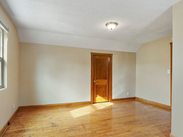 unfurnished room featuring light hardwood / wood-style floors, vaulted ceiling, and a textured ceiling