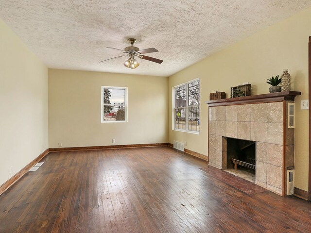 unfurnished living room with a tiled fireplace, ceiling fan, a textured ceiling, and dark hardwood / wood-style flooring