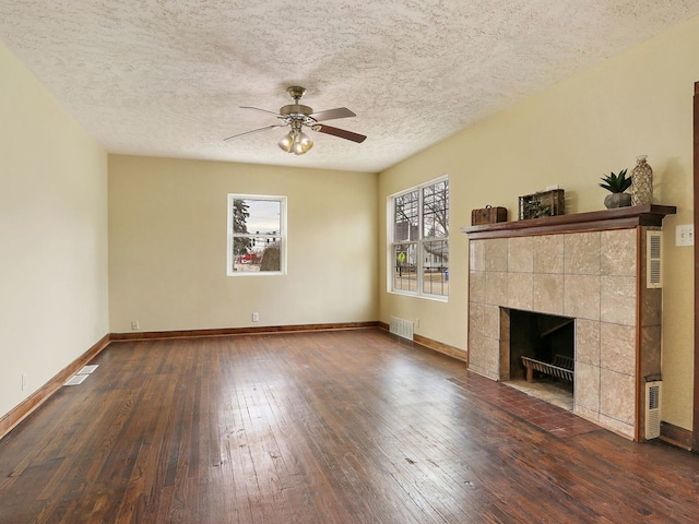 unfurnished living room featuring a tiled fireplace, a textured ceiling, dark hardwood / wood-style floors, and ceiling fan