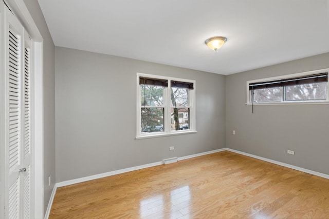 unfurnished bedroom featuring baseboard heating, a closet, and light wood-type flooring