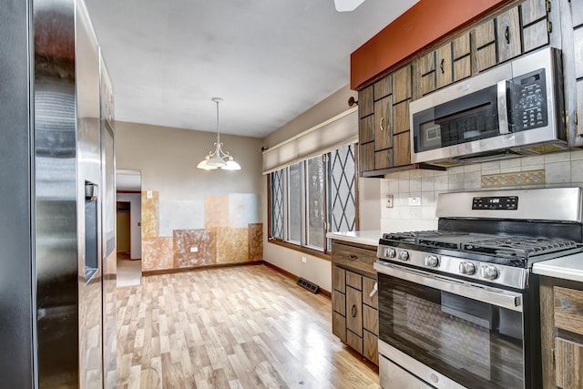 kitchen featuring tasteful backsplash, stainless steel appliances, light countertops, light wood-type flooring, and a notable chandelier