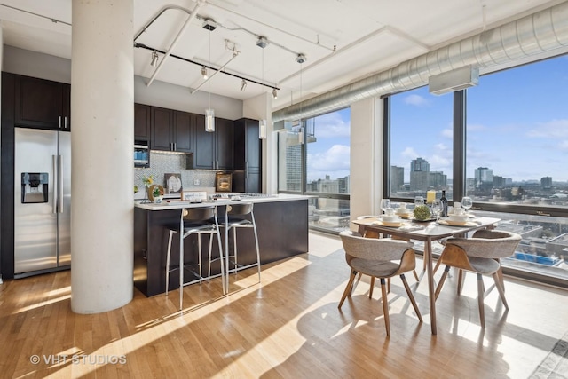 kitchen featuring a kitchen breakfast bar, decorative backsplash, stainless steel fridge with ice dispenser, track lighting, and light hardwood / wood-style flooring