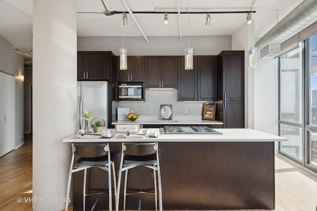 kitchen featuring appliances with stainless steel finishes, hanging light fixtures, dark brown cabinets, decorative backsplash, and light wood-type flooring