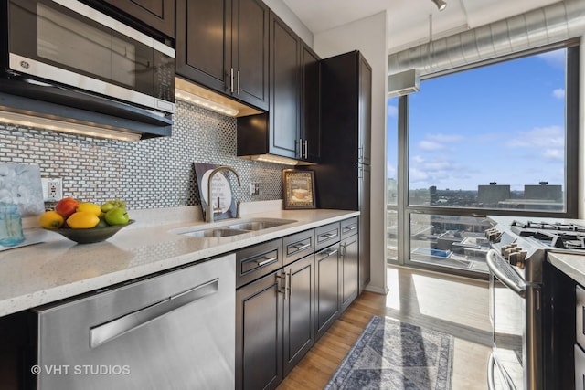 kitchen with dark brown cabinetry, sink, light stone counters, stainless steel appliances, and backsplash