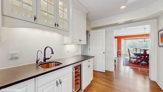 kitchen featuring sink, wine cooler, white cabinets, a chandelier, and light hardwood / wood-style flooring