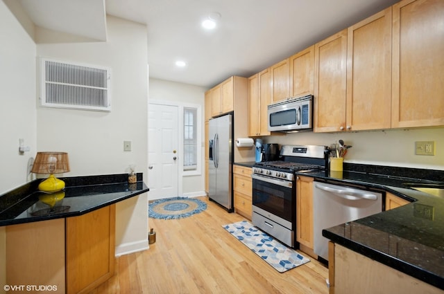 kitchen with appliances with stainless steel finishes, light brown cabinetry, light hardwood / wood-style flooring, and dark stone counters