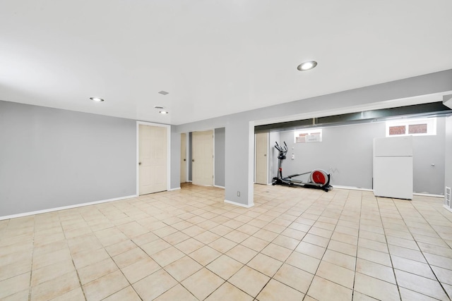 basement with light tile patterned floors and white refrigerator