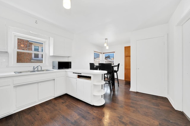 kitchen with decorative light fixtures, sink, white cabinets, dark hardwood / wood-style flooring, and kitchen peninsula