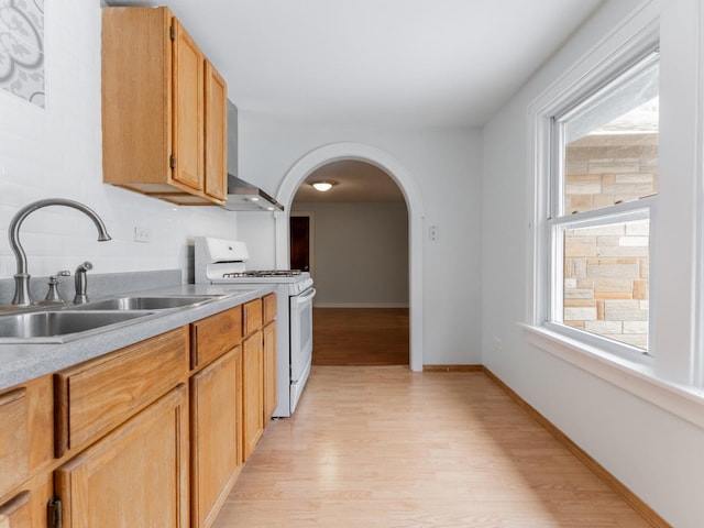 kitchen with sink, white gas stove, backsplash, wall chimney exhaust hood, and light wood-type flooring