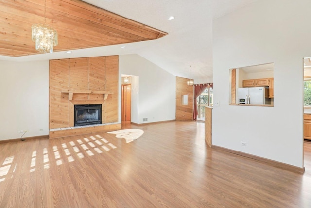 unfurnished living room featuring an inviting chandelier, high vaulted ceiling, a tile fireplace, and light hardwood / wood-style floors