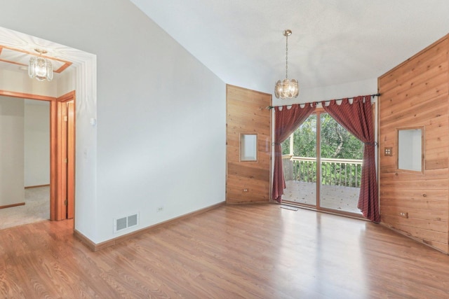 empty room with a notable chandelier, wood-type flooring, and wood walls