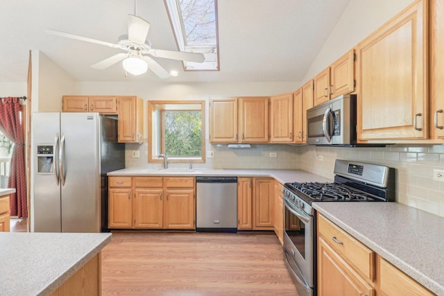 kitchen featuring light brown cabinetry, stainless steel appliances, light hardwood / wood-style floors, and vaulted ceiling with skylight