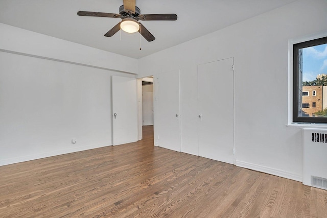 unfurnished bedroom with hardwood / wood-style flooring, ceiling fan, and radiator heating unit