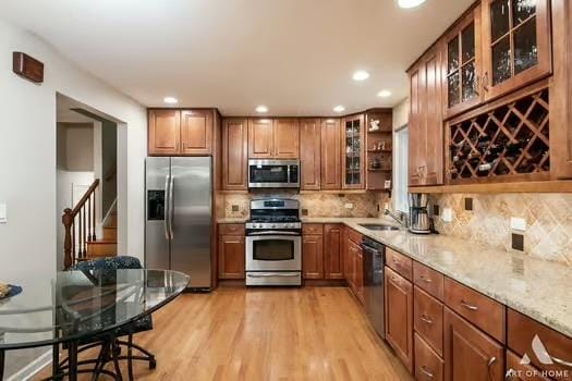 kitchen featuring appliances with stainless steel finishes, tasteful backsplash, sink, light stone countertops, and light hardwood / wood-style flooring