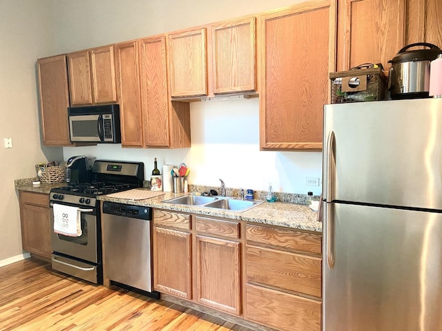 kitchen with light stone counters, sink, light wood-type flooring, and appliances with stainless steel finishes