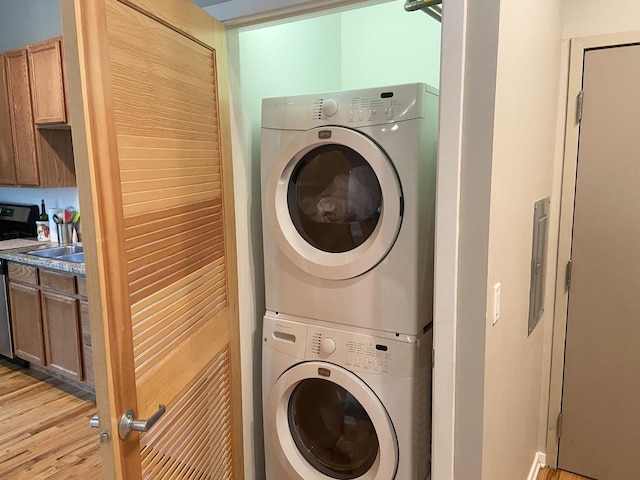 laundry room featuring stacked washer and dryer and light hardwood / wood-style flooring