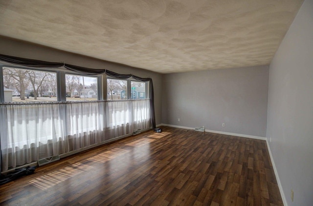 empty room featuring a textured ceiling, dark wood finished floors, and baseboards