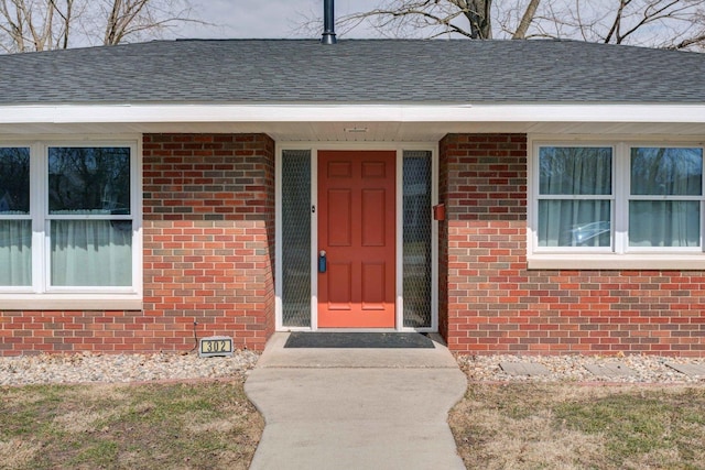 entrance to property with roof with shingles and brick siding