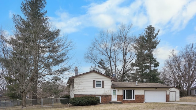 split level home featuring a garage, brick siding, fence, driveway, and a chimney