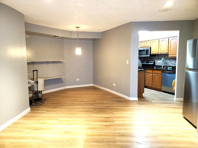 kitchen featuring pendant lighting, sink, appliances with stainless steel finishes, light hardwood / wood-style floors, and decorative backsplash