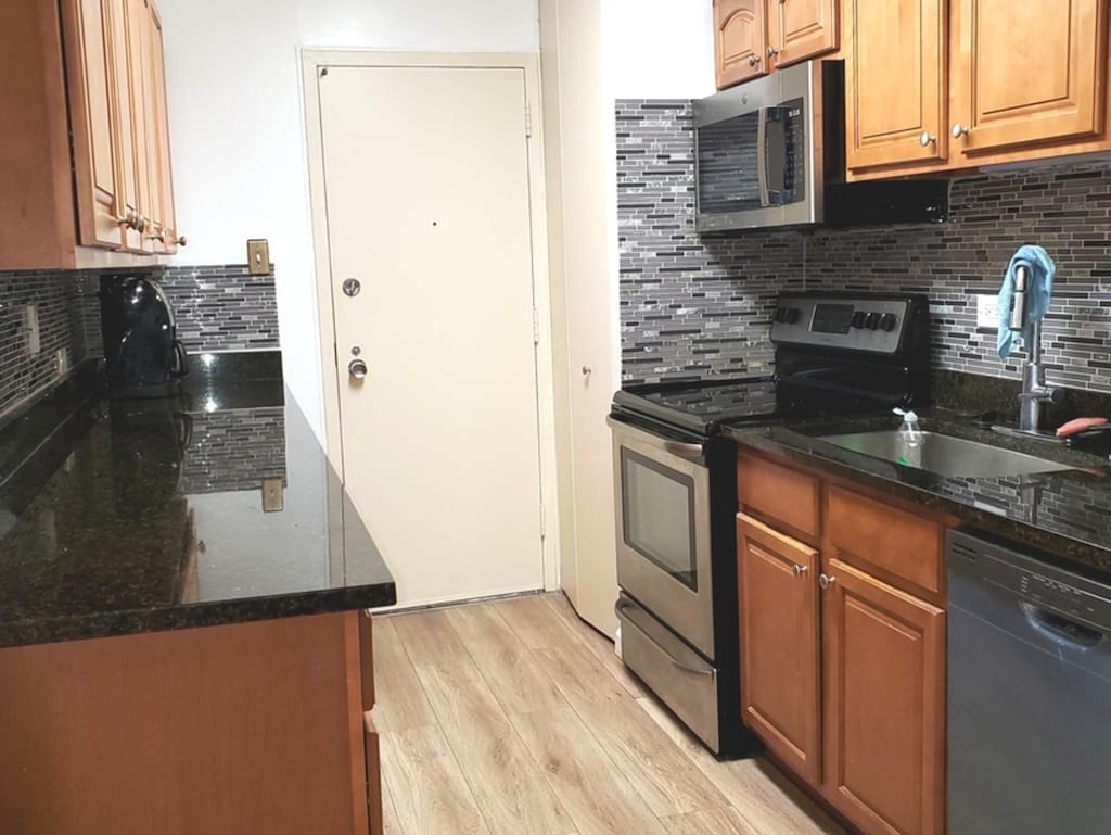 kitchen with sink, light hardwood / wood-style flooring, dark stone countertops, stainless steel appliances, and backsplash