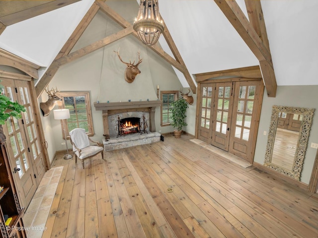 unfurnished living room with beamed ceiling, a stone fireplace, light wood-type flooring, and french doors