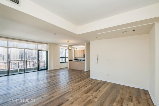 unfurnished living room with an inviting chandelier, floor to ceiling windows, and dark hardwood / wood-style flooring