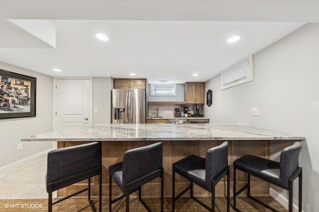 kitchen with a kitchen bar, stainless steel fridge, kitchen peninsula, and decorative backsplash