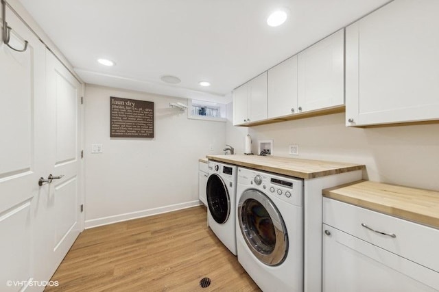 washroom featuring washing machine and dryer, cabinets, and light wood-type flooring