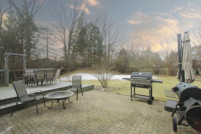 patio terrace at dusk with a water view, area for grilling, a yard, and an outdoor fire pit