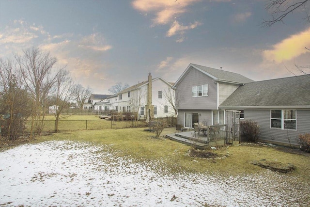 snow covered back of property featuring a wooden deck and a lawn