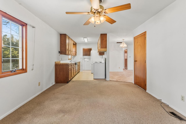 kitchen featuring washing machine and clothes dryer, ceiling fan, light colored carpet, brown cabinets, and stove