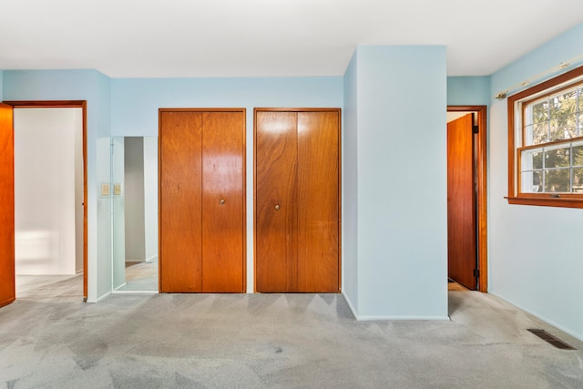 unfurnished bedroom featuring visible vents, multiple closets, and carpet