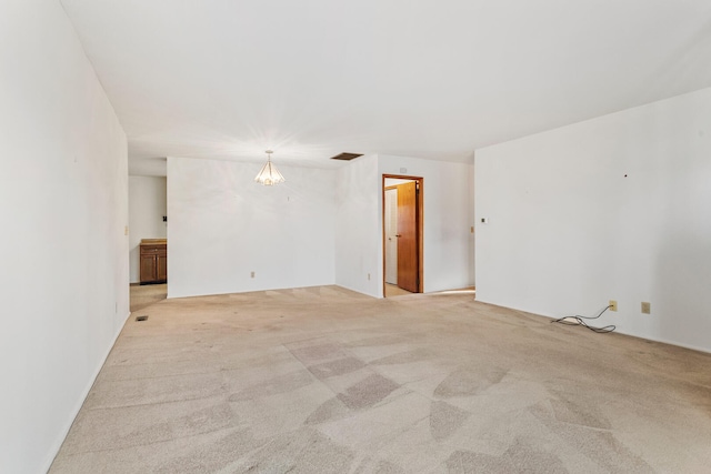 empty room featuring a notable chandelier, light colored carpet, and visible vents