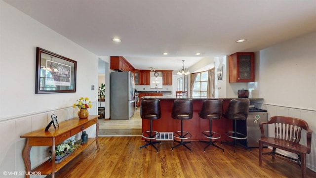 kitchen featuring a wainscoted wall, a peninsula, freestanding refrigerator, and wood finished floors