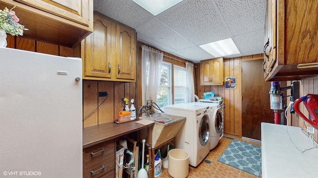 clothes washing area featuring washer and clothes dryer, wooden walls, and cabinet space