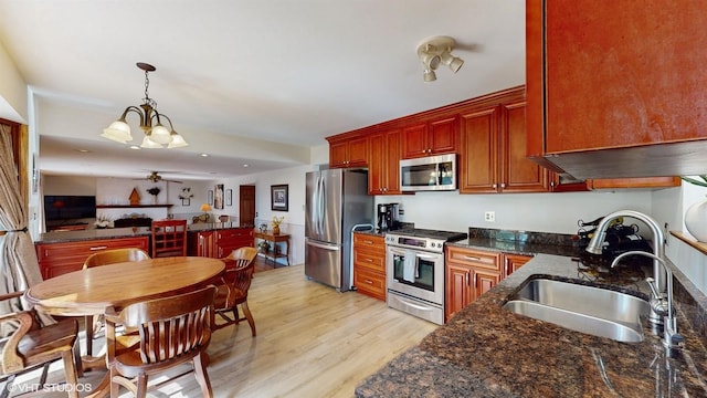 kitchen with pendant lighting, ceiling fan with notable chandelier, light wood-style flooring, stainless steel appliances, and a sink