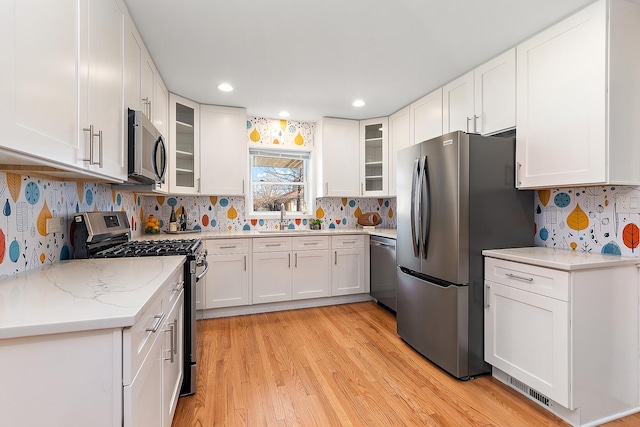 kitchen featuring sink, light hardwood / wood-style flooring, appliances with stainless steel finishes, light stone countertops, and white cabinets