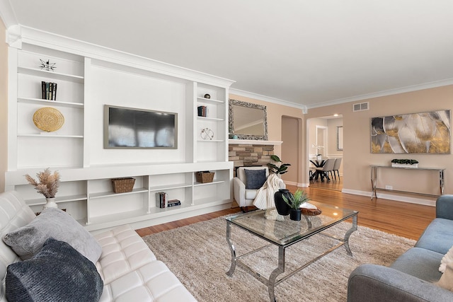 living room featuring crown molding, a fireplace, light hardwood / wood-style floors, and built in features