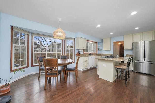 kitchen featuring dark wood-type flooring, stainless steel refrigerator, a center island, light stone counters, and decorative light fixtures