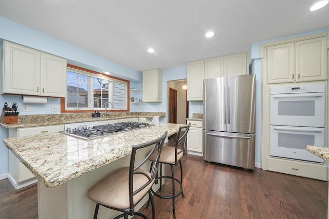 kitchen with a breakfast bar area, dark hardwood / wood-style flooring, a kitchen island, stainless steel appliances, and light stone countertops