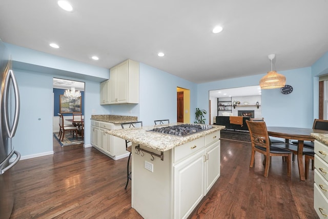 kitchen featuring dark wood-type flooring, appliances with stainless steel finishes, a kitchen island, a kitchen bar, and decorative light fixtures